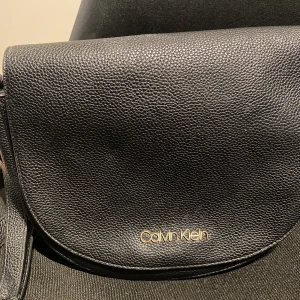 Calvin Klein väska  - Svart väska från Calvin Klein. Stängs med lock. Många fack. Lång axelrem. 