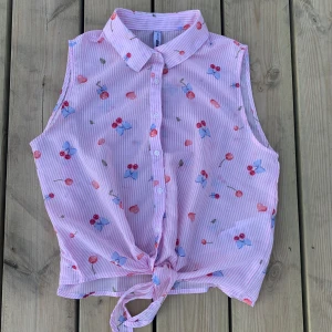 Fräsch ärmlös sommarblus  - Säljer en armlös tunn sommarblus som är ljusrosa randig med körsbär, hjärtan och blad på. Den knyts längst ner och har en krage upptill.  Använd fåtal gånger och är nästintill nyskick! STORLEK XS. Skicka privat vid frågor  ❌ANVÄND INTE KÖP DIREKT❌ 