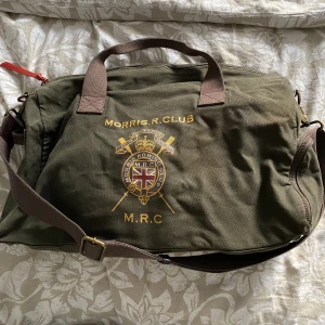 Morris väska - Väldigt snygg morris axelremväska i mörkgrön färg med brun axelrem.  Morrismärke på ena sidan av väskan som ni ser på bild.  Lite mindre än en ”weekend bag”  Skriv om ni har frågor eller vill ha mer bilder.