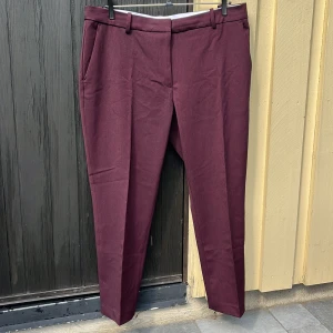Mörkröda kostymbyxor - Ett par fina, mörkröda kostymbyxor i fint skick. Har två fungerande framfickor och en stängning med byxkrok, knapp och dragkedja. 68% polyester 28% viskos 4% elastan.