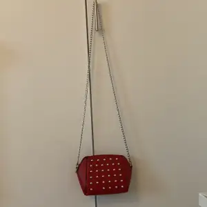 En vinröd Cross-body väska med studs på, en stud saknas men syns knappt 