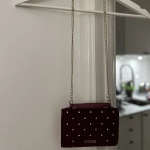Liten väska från Guess  - Väska/plånboksväska i en vinröd färg från Guess med nitar/pärlor. Använd 2 gånger. 