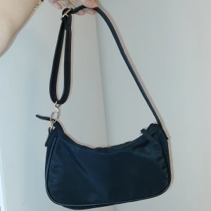 Svart handväska - Söt svart väska från Even&Odd. Materialet är Polyester och den är i utmärkt skick (ingen skada på materialet). Har använt den som utgångväska eftersom den får plats med allt som behövs men passar också på stan eftersom den väger lite! 2 dragkedjefickor.