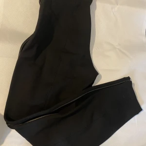 Leggings med läder detalj  - Svarta högmidjade petite leggings ifrån vila med fina läder detaljer vid midjan och vid sidan av byxan, passformen är kostymaktig men sitter väldigt tajt, det är en S men tycker en xs passar bättre då den var liten i storlek! Ny med prislapp kvar