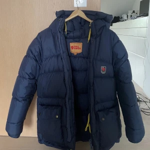 Fjällräven jacka  - Marinblå fjällräven jacka i den tjockare modellen. Den är i storlek xxxs men passar som en vanlig xs. Köpt förra året så fortfarande i fint skick. Har en reva i ena armen. Bara rimliga bud tack!🥰