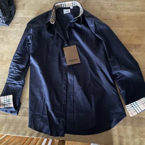 Burberry skjorta - En oanvänd marinblå burberry skjorta i storlek M. Tags sitter på och nedkommer. Vid funderingar eller fler bilder är det bara att skriva. Priset går att diskutera vid snabb affär. 