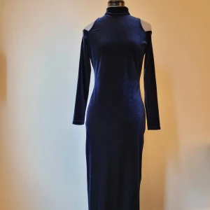 Lång sammetsklänning - Lång aftonklänning i midnattsblå stretchigt sammetstyg. Långärmad med cut outs över axlarna, polokrage som knyts i nacken och slits bak på kjolen. Sömmen i öppningen i ryggen har gått upp lite, vilket syns på sista bilden. I övrigt är klänningen i väldigt