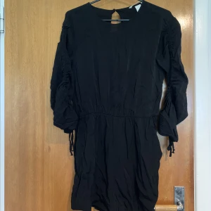 Svart playsuit - Svart playsuit från hm med rynkade detaljer på armarna. Playsuiten har fickor och är delvis öppen i ryggen. Fint skick.