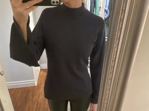 Tröja med högre krage och slits - Mörkgrå (nästan svart) tröja. Lite högre krage, vida armar och slits både på sidorna och armarna. Finns öglor till skärp som jag tappat bort, så man kan antingen klippa bort öglorna eller ta annat skärp. Bra skick!