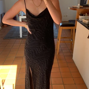 Svart långklänning  - Svart långklänning med mörkt zebra mönster i satinliknande material 