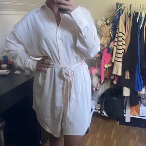 Vit skjortklänning  - En snygg och elegant skjortklänning som är lite oversized. Passar både storlek 38/40. Ett band kommer till för att kunna spänna åt vid midjan och forma kroppsformen. Aldrig använd, prislappen är fortfarande på! 