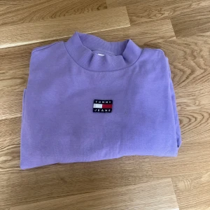 Sweatshirt ifrån Tommy Jeans - En snygg lila croppad sweatshirt ifrån Tommy Jeans i storlek L. En pytte pytteliten fläck som knappt syns.  Kan skicka mer bilder vid intresse. 