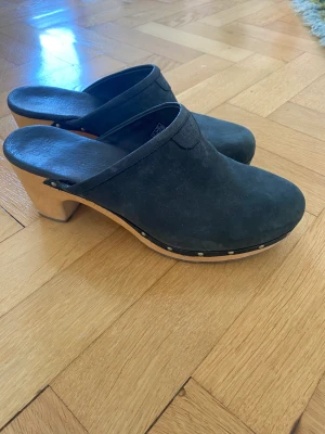 Träskor från UGG - Jättefina svarta träskor i läder från märket UGG.  Säljer för att jag inte använder dem. De är i fint skick men har en liten spricka i trät (kolla bild 3). Dock inget som påverkar skorna i övrigt och inget jag lagt märke till förrän nu. 100 kr+ frakt