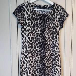 Längre tight leopardklänning - Leopardklänning i slimfit model med kortärm, Material i polyester. Längden går ner nedan knäna. 