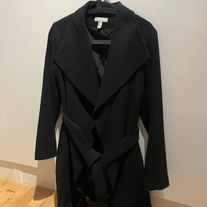 Kappa Svart strl S - Säljer denna svarta kappa med bälte från HM. Perfekt till höst och vår! Storlek S, är i nyskick och är INTE nopprig. Passar S och XS