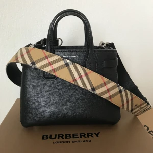 Burberry väska  - Burberry ”Banner” väska i fint skick. Kvitto, dustbag, presentband samt kartong medföljer. Justerbar axelrem med klassiskt burberry mönster på. Spårbar frakt inkluderas i priset via postnord. 