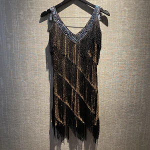 Klänning - En guldig charleston klänning med svarta fransar som även utsmyckad med paljetter i urringningen. Klänningen är perfekt för halloween eller annat event där du ska vara finklädd! I storlek L, men den passar S och M då klänningen ska vara lite over-sized