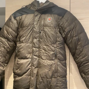 Fjällräven jacka  - Säljer nu min brun/gröna fjällräven då den blivit för liten för mig, den är i hyffsat gott skick med allt dun kvar, men två mindre lagningar som ej syns när jackan är på och ludd på kardborrebanden men som lätt kan tas bort, där av priset