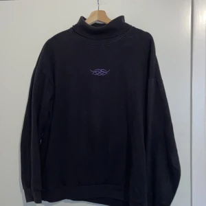 OverSiezed TurtleNeck - OverSiezed TurtleNeck Med En Lila Broderad Symbol På Bröstet  Storlek: M (OverSiezed) Skick: Medel, Svag Missfärgning Runt Halsen