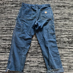 Carhartt blå Carpenters dungaree fit - Hej! Säljer ett par Carhartt carpenters då jag inte längre använder de. De är i relativt bra skick om man bortser från färg stänket. Det går säkert att få bort en del i tvätt.  Storlek 36/34