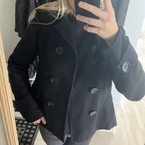 Svart kort kappa - Svart kort kappa. Den är i storlek 40. Använd fåtal gånger, fina skick inga defekter. Yttertyget är 30% ull 70% polyester.