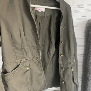 Grön jacka - mörkgrön jacka som passar både under vår och höst men också sommar!  Fina gulddetaljer vid ärmar, knäppning och fickor. I fint skick men lite defekter därav priset ❣️