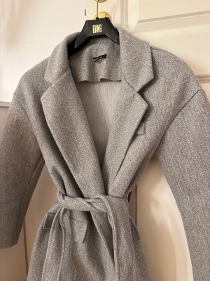 Grå kappa - Grå kappa med knappar och snörning i storlek 34. 