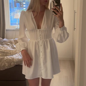 Klänning - Vit klänning med knappar och korsett liknande midja, helt perfekt till studenten!! Endast använd en gång på min egen student, så som ny! Kan mötas upp i Jönköping eller Vaggeryd annars tillkommer fraktkostnad 🤍