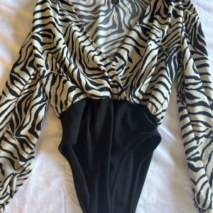 Blus-body - Väldigt tunt material, randig i svart och beige. (Body). Blus/skjorta. Vid frakt betalar konsumenten.