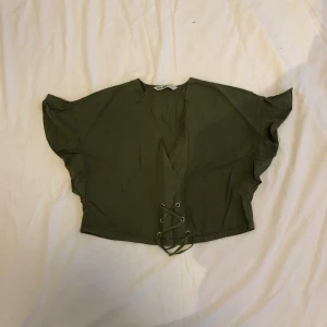 Grön croptop - Grön croptop med volang vid armarna, snörningen i midjan ger en korsett-effekt. Köpt från Zara, strl S. Köparen står för frakten :)