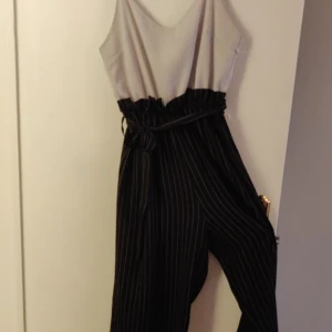 Jumpsuit - Svart och grå jumpsuit, vadlånga ben. Tajt upptill och flowie byxor. Band i midjan och dragkedja i bak. Axelbanden är ställbara efter eget tycke. 😁 Kika gärna in vad mer jag säljer! 💞