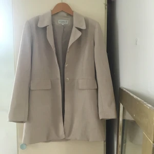 Vintage-kavaj 80-tal - Beige vintage/80tals-kavaj, med en aning vadderade axlar. Väldigt bra skick, köpt second hand. Storlek 38. Längd: 79 cm. Kavajen är tunn så passar perfekt nu till sommaren :) 