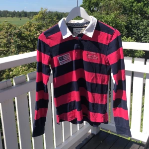 Bomullsskjorta Bondelid - Blå och rosa randig bomullsskjorta från bondelid med vit krage. Bondelidmärken på båda sidor om knapparna. Lite missfärgning på insidan av kragen.