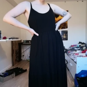 Svart långklänning - Enkel svart långklänning, perfekt om man vill ha en mysig kofta över och se ut som en höstdröm eller ha coola accessoarer till och se ut som en festivaldröm. Storlek M men lite oversized så skulle nog sitta fint på någon med L! Frakt tillkommer 