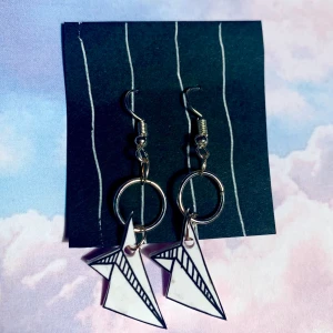 Paper plane vita örhängen  - Vita små pappersflygplan i krympplast☺️ nickelfria krokar, nya re-inforced ringar, vit baksida. Flera finns inne! Frakt 11kr