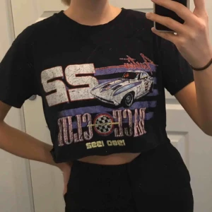  - En svart kort t-shirt som går över naveln. Tröjan är i bra skick och har ett coolt tryck!! 