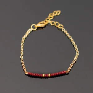  - Handgjort armband i guld och mörkröd. Kedjan är justerbar. OBS guldfärgen är inte lika gul/orange som på bilden.  Fri frakt vid köp över 100:-.