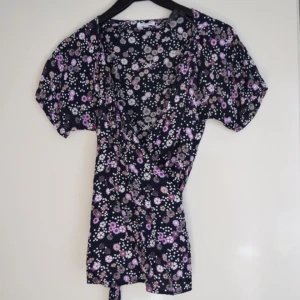  - Omlottblus med märke STOCKHLM i strl 38. Fint blommönster med lila färger. Gott skick.