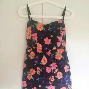  - Svart/blommig kort klänning i storlek 34. Ribbning och dragkedja i ryggen. Justerbara axelband.  Endast använd ett par gånger. I mycket bra skick!