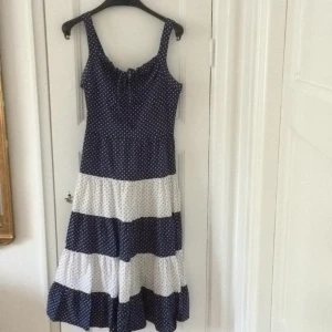  - Fantastisk klänning med härlig vidd i kjolen. Den har tyvärr blivit för liten för mig. Litet knyt framtill. Baktill en dragkedja och knappar, se bilder. Dock kan knapparna med fördel bytas ut, så att det blir mer enhetligt. Fint skick i övrigt. 
Räcker mig till knäna, jag är 173 cm.