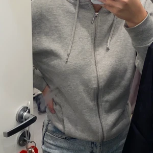 Grå hoodie - En grå mysig hoodie med silver dragkedja, använd 3-4 gånger och är i storlek 34 men passar andra storlekar också.