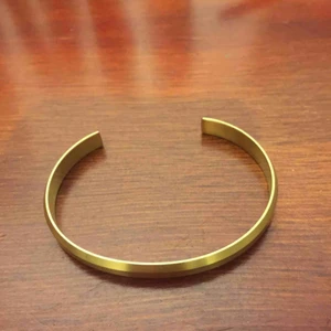  - Stelt armband i 18K guldpläterat rostfritt stål med borstad yta och profilerad kant. Armbandet är ca 7 mm brett och 19 cm i omkrets. Det kan försiktigt formas om för att passa just din handled.