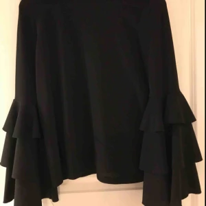  - Svart topp/blus med vida ärmar med volanger. Stretchigt material, så passar nog även en mindre M. Superfin både till vardags och till fest men är tyvärr för liten för mig. Plagget är i mycket gott skick trots flitigt användande!