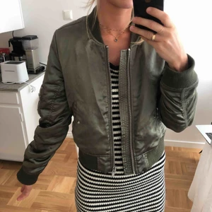  - Glansig grön bomberjacka från Gina tricot. Bra skick förutom liten fläck fram men som man knappt ser, se sista bilden.   Köparen står för frakt alternativt kan vi mötas upp i Stockholm ☺️