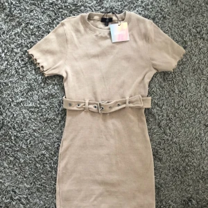  - Beige stretchig klänning med skärp i midjan. Storlek 38.