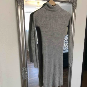  - Grå finstickad klänning med hög hals.