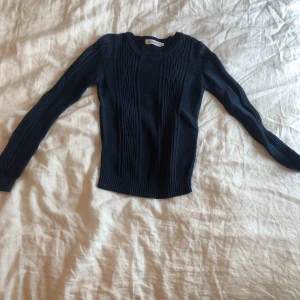  - Blå kabelstickad tröja som är figursydd och passar lika bra på en uppklädd middag och hemma. 