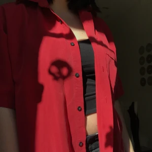 röd skjorta - jättehärlig röd t-shirt skjorta i ett ganska levande material, den är väldigt lätt och skön att ha på sig. perfekt att slänga på sig över en tshirt nu i sommar!