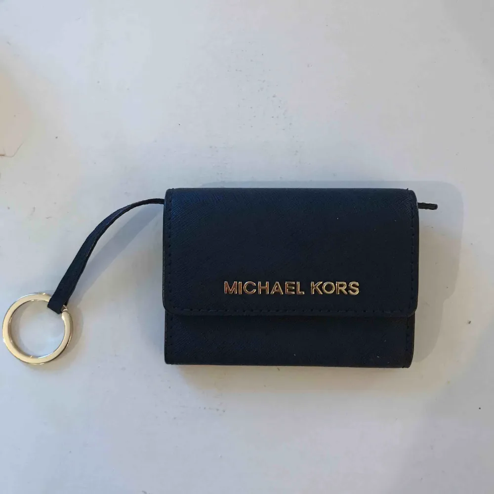 Säljer en mörkblå plånbok från MK med guldiga detaljer. Knappt använd. Mått ca: 11 cm bred & 8.5 cm hög. Priset är ink frakt!. Accessoarer.