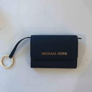 Säljer en mörkblå plånbok från MK med guldiga detaljer. Knappt använd. Mått ca: 11 cm bred & 8.5 cm hög. Priset är ink frakt!